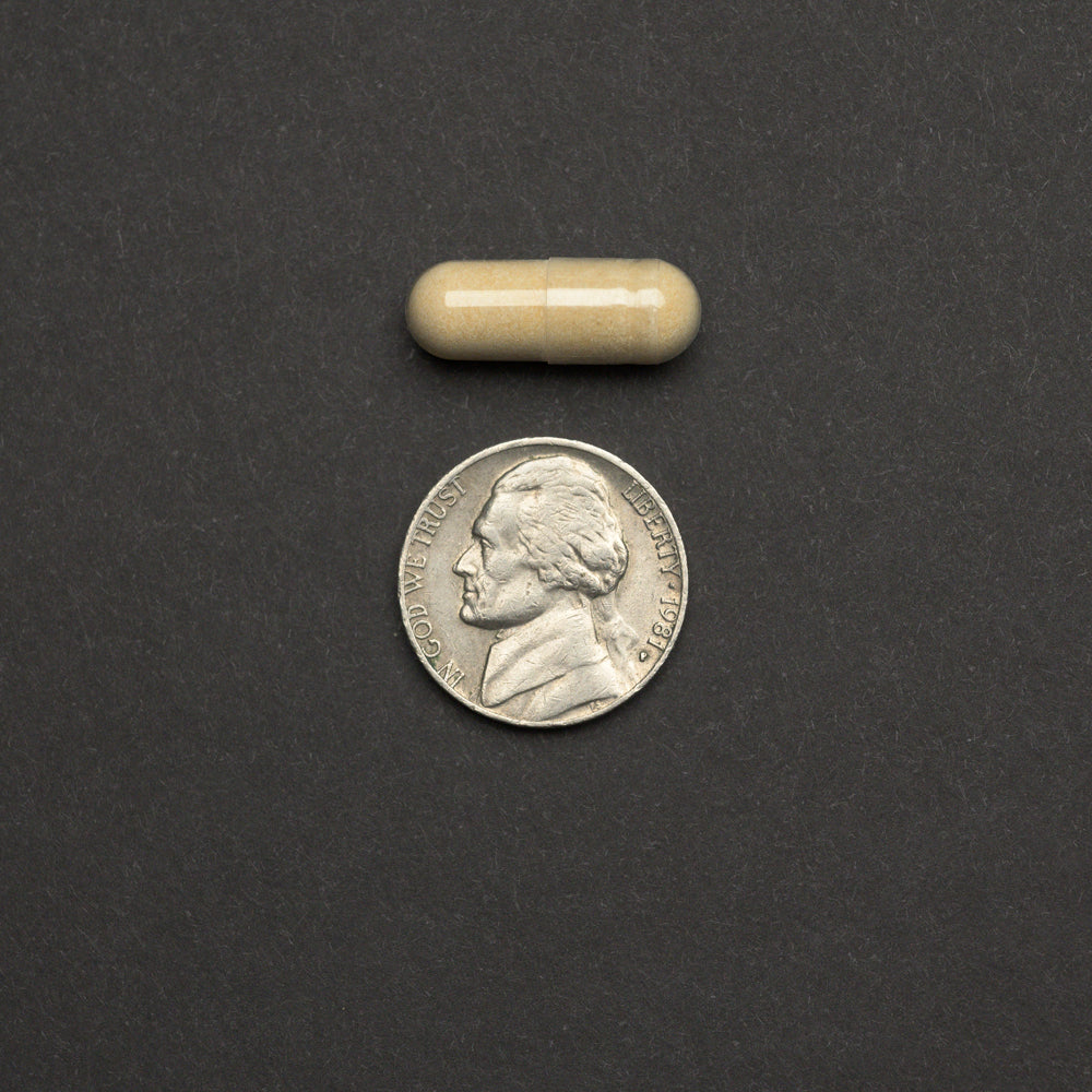 Beige capsule next to a nickel on a dark gray background