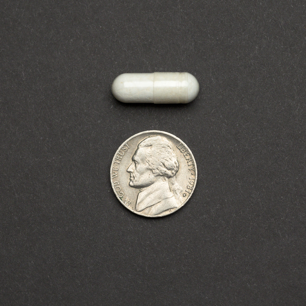 White capsule next to a nickel on a dark background