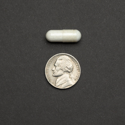 White capsule next to a nickel on a dark background