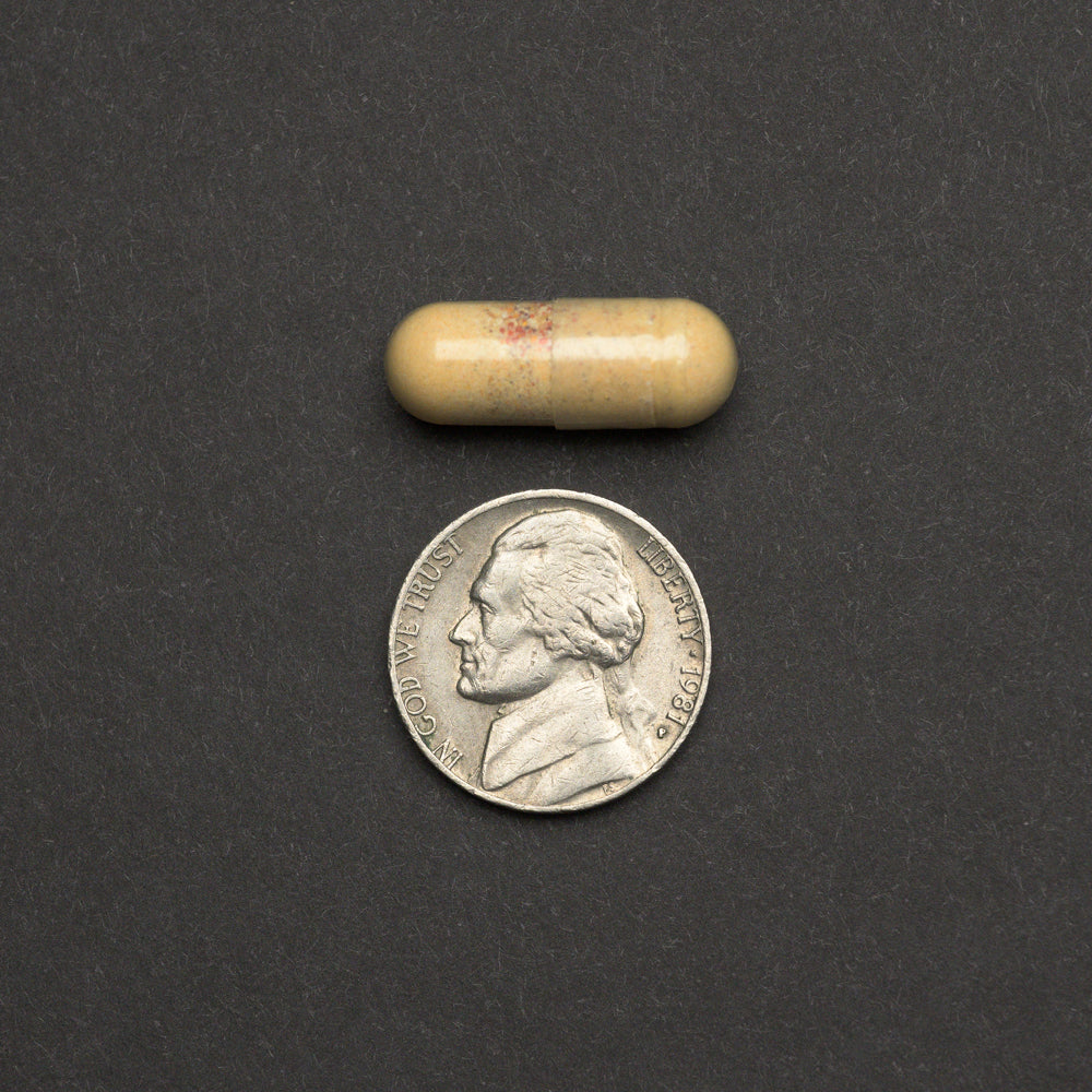 Beige capsule next to a nickel on a dark background